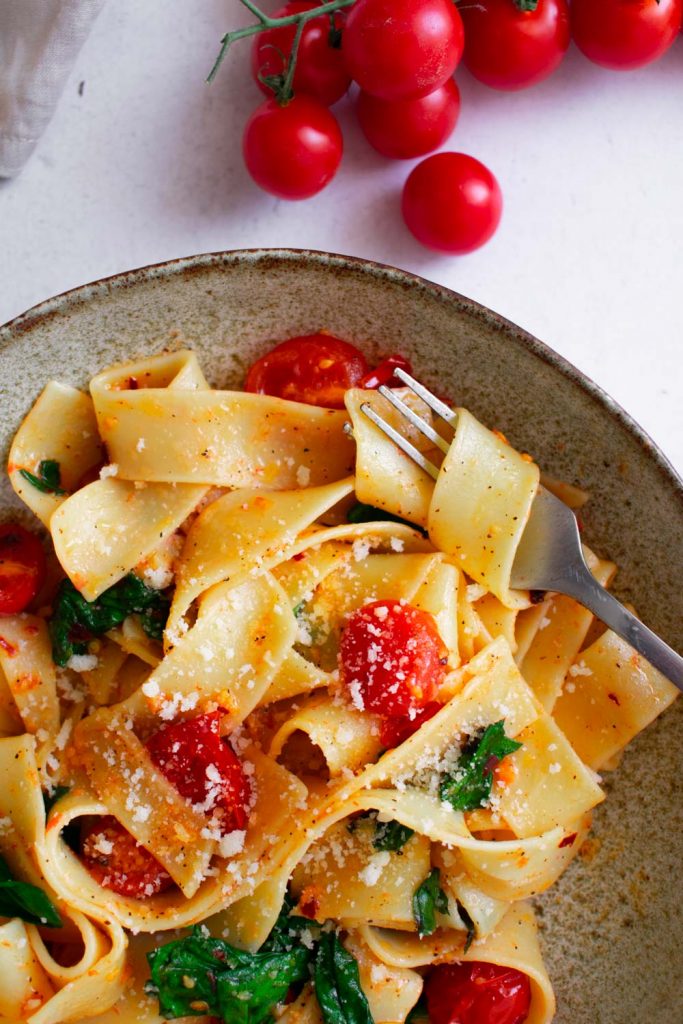 a plate of pappardelle pasta with spinach and tomatoes.