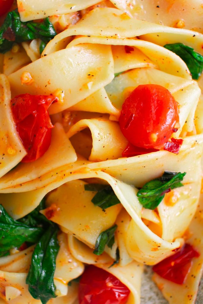 a close up of pasta with spinach and tomatoes.