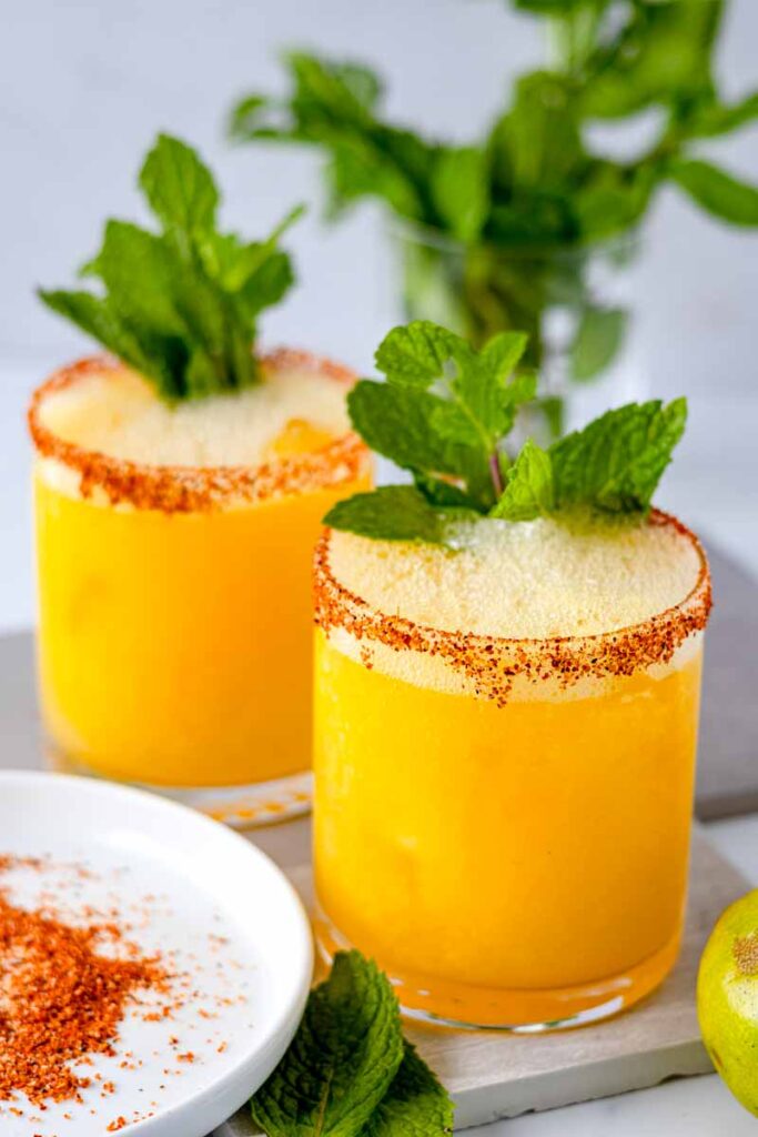 two glasses of mango Moscow mule mocktails with mint leaves on a marble table