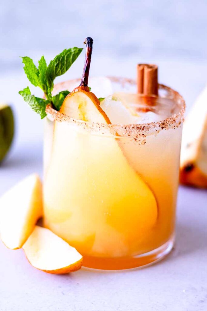 a glass of Pear Ginger Beer Mocktail with slice of pear, mint and cinnamon stick garnish on tabletop
