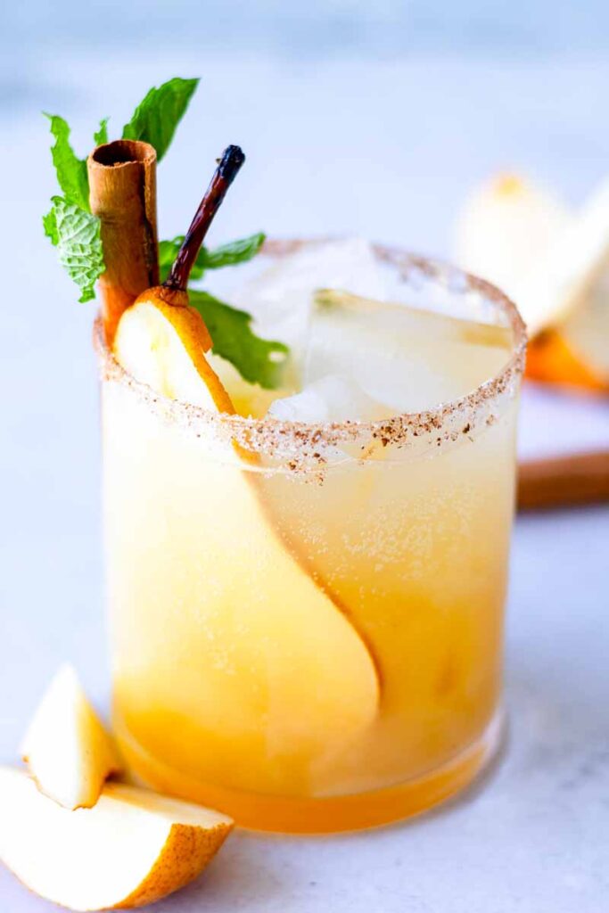 a side view of pear ginger beer mocktail with a garnish of sliced pear, ice, mint leaves and cinnamon stick