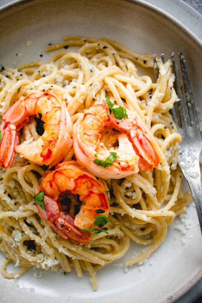a plate of cacio e pepe in a plate with shrimps on top and fork placed on the side