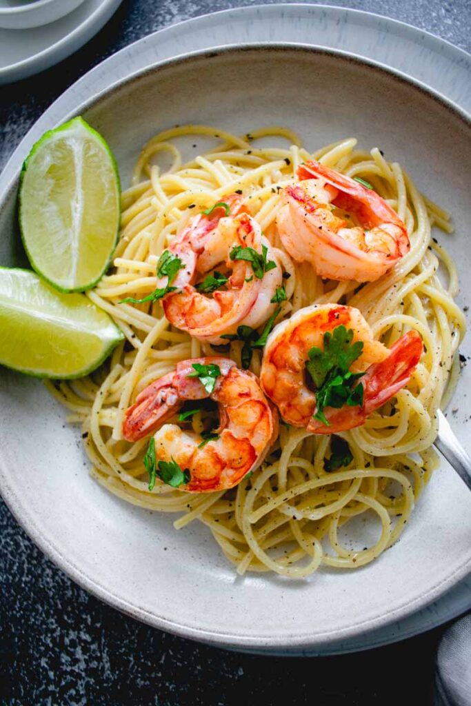 cacio e pepe pasta dish with four shrimp and two lime wedges on the side
