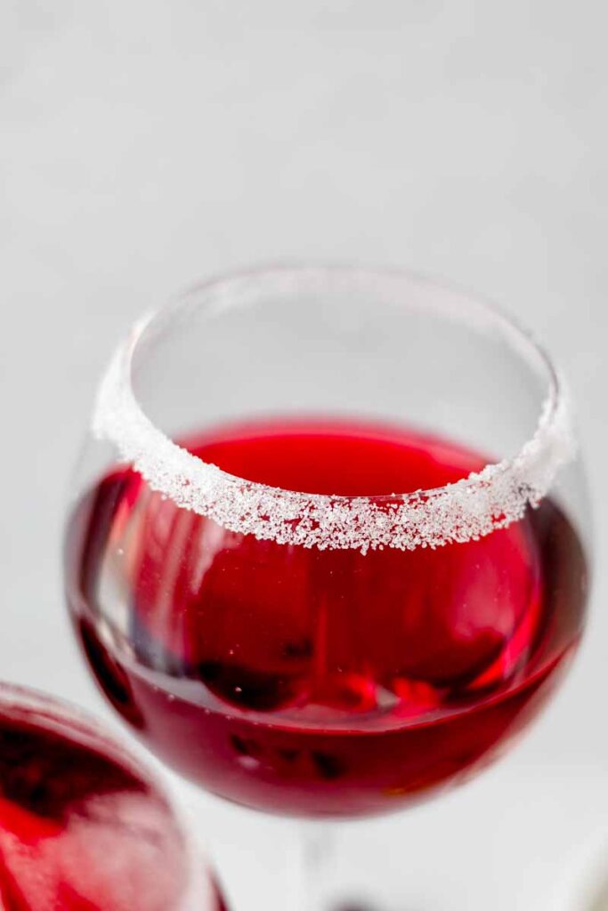 a drinking glass with cranberry juice inside rimmed with white sugar 