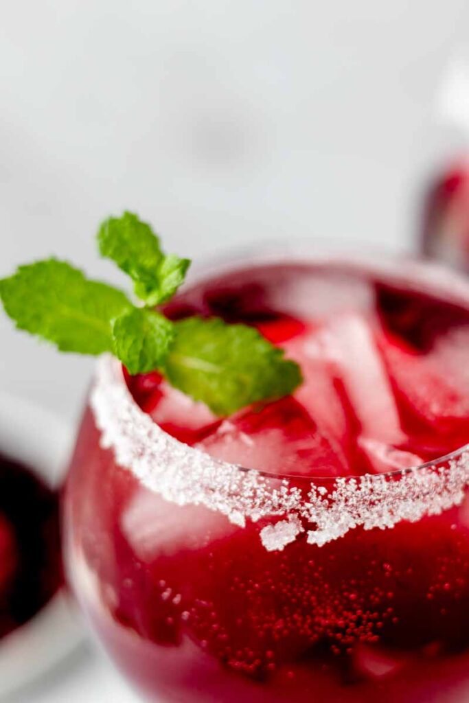 a glass of cranberry mocktail with mint garnish and sugar on the rim
