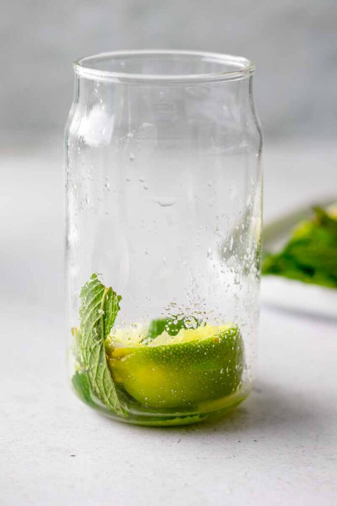 a glass with lime wedges, white sugar, mint leaves muddled altogether