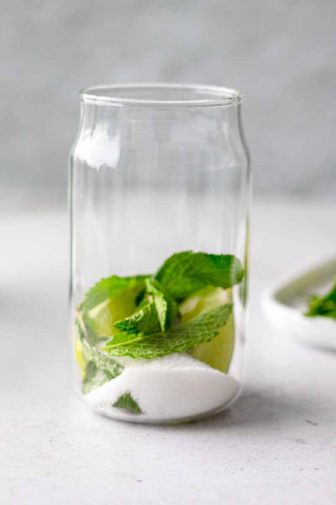 a glass with lime wedges, white sugar, mint leaves ready to be middled to make virgin mojito drink