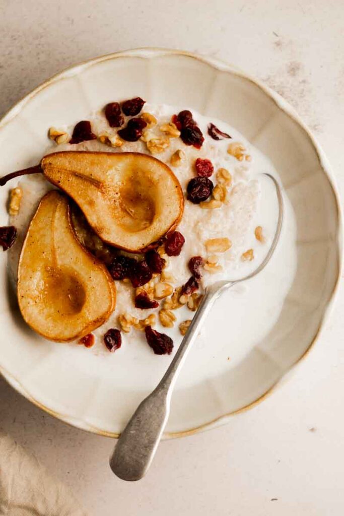 baked pear oatmeal served in a dish with milk splashed on top and cranberries and walnut