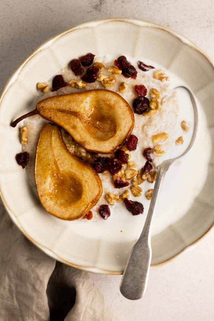 a bowl of oatmeal with two baked pears on top and dried fruits and nuts